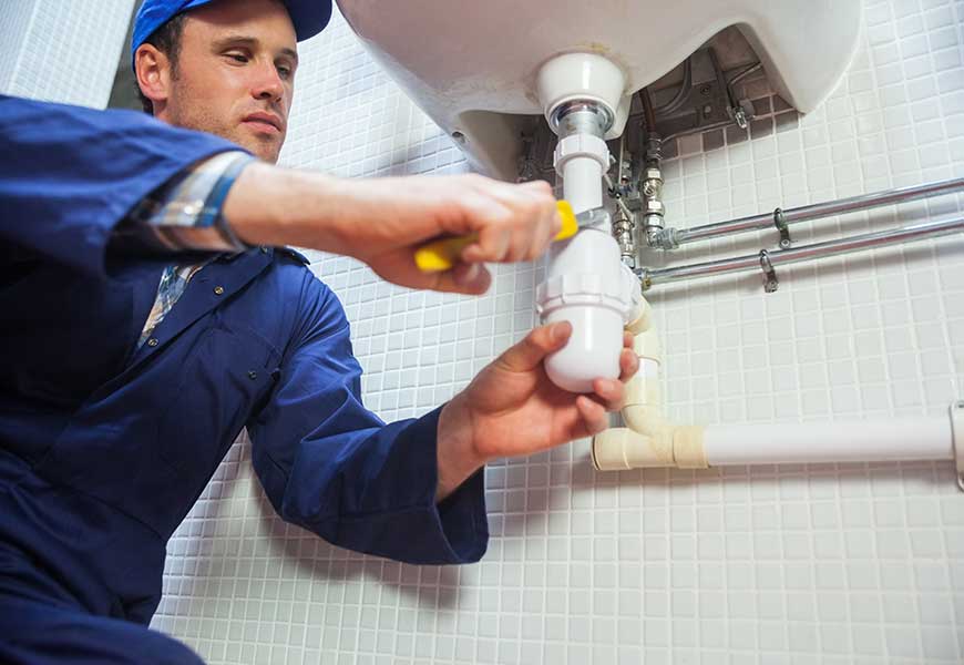 Frowning plumber repairing sink in public bathroom